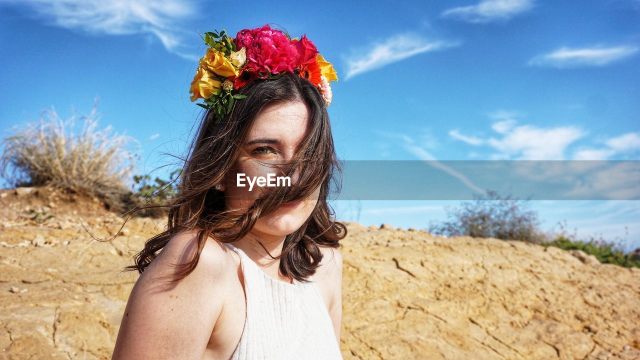 Portrait of young woman with pink flowers against sky