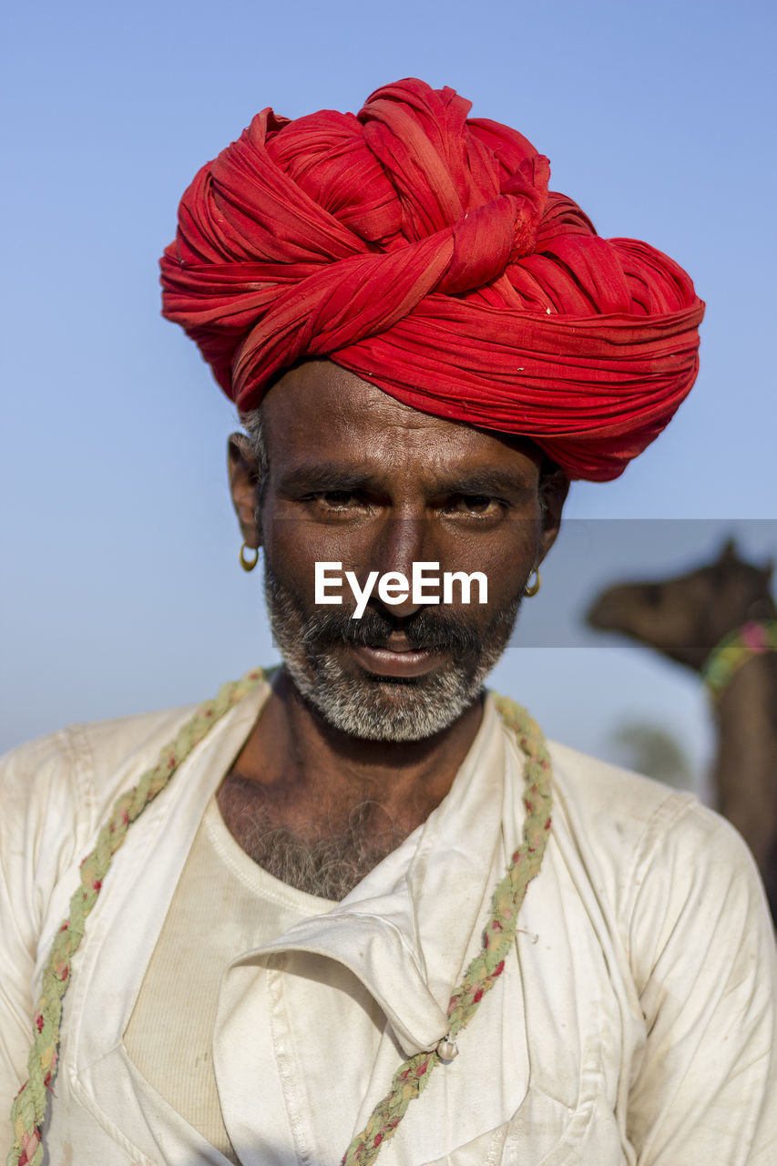 Close-up portrait of man wearing red turban against clear sky