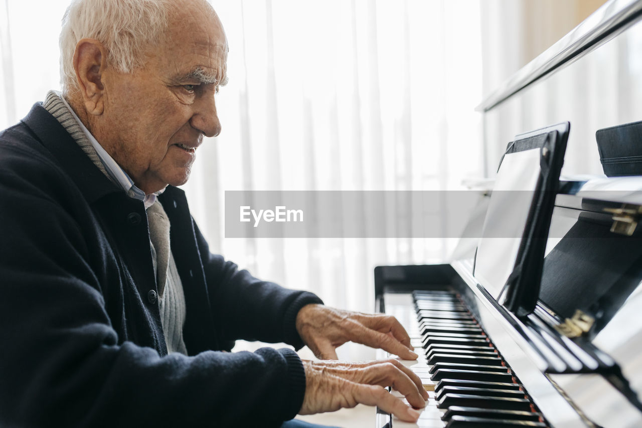 Senior man sitting in wheelchair playing piano at home