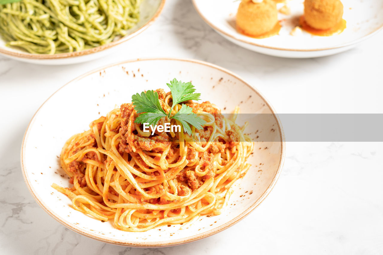 Delicious dishes of italian gastronomy on white marbled board and gray background. pasta bolognese