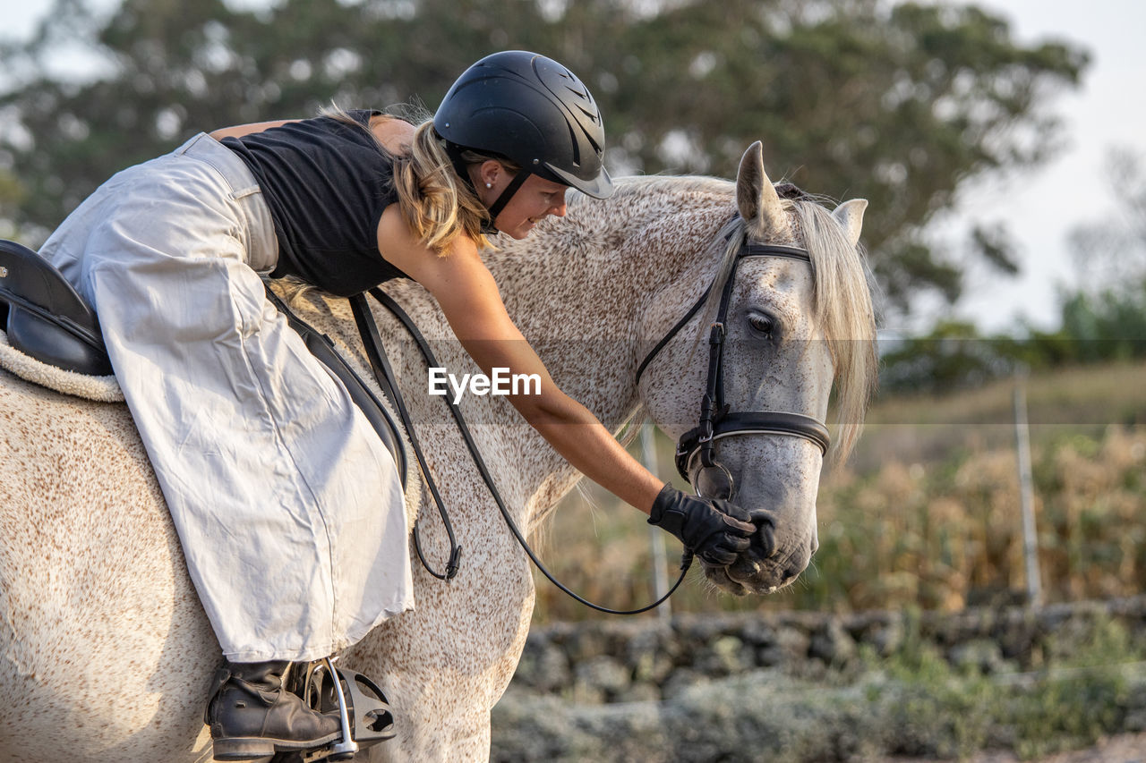 White lusitano mare, female dressage rider, outdoors on sand.