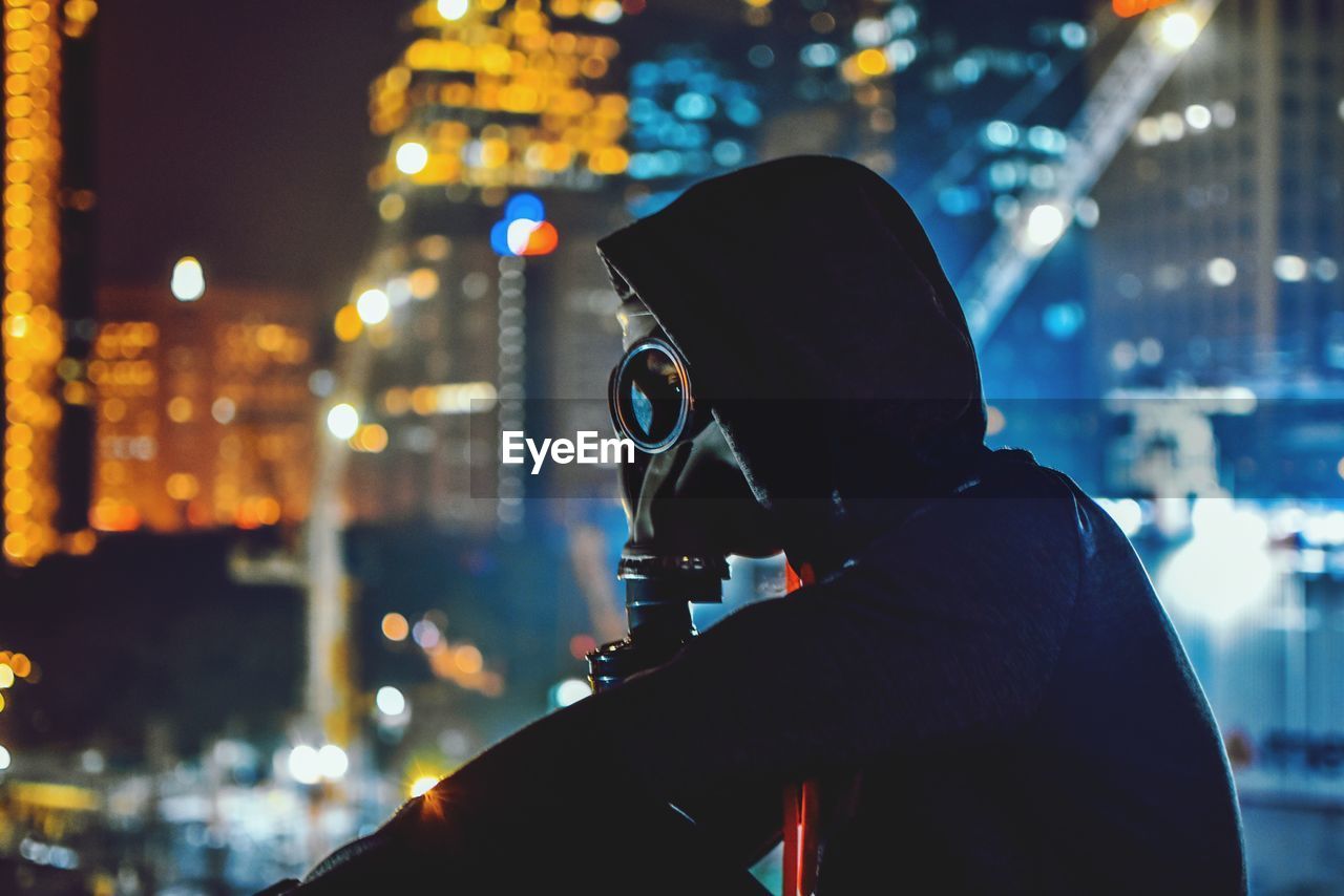 Side view of man photographing against illuminated buildings at night