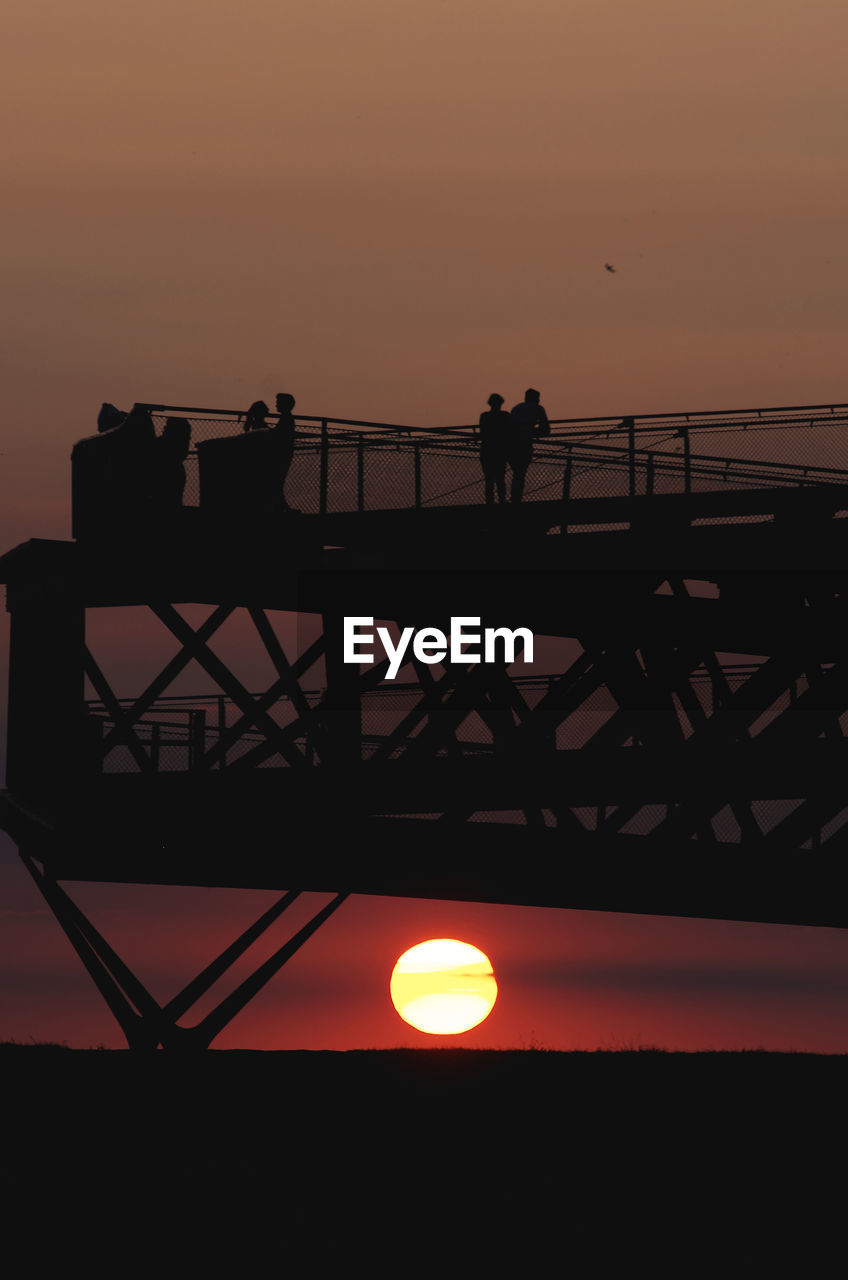 SILHOUETTE PEOPLE STANDING BY RAILING AGAINST SEA DURING SUNSET