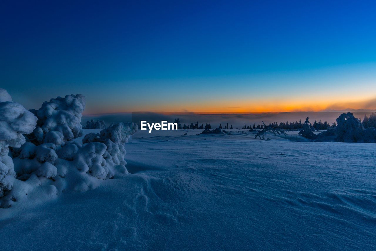 Scenic view of snow covered field against sky during sunset