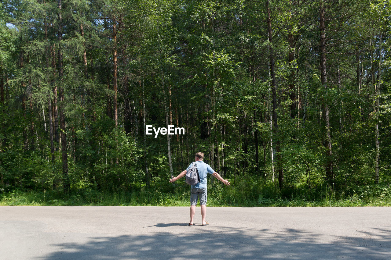 Full length of man standing on road amidst trees in forest