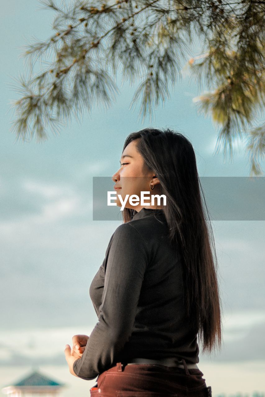 Young woman looking at camera against sky