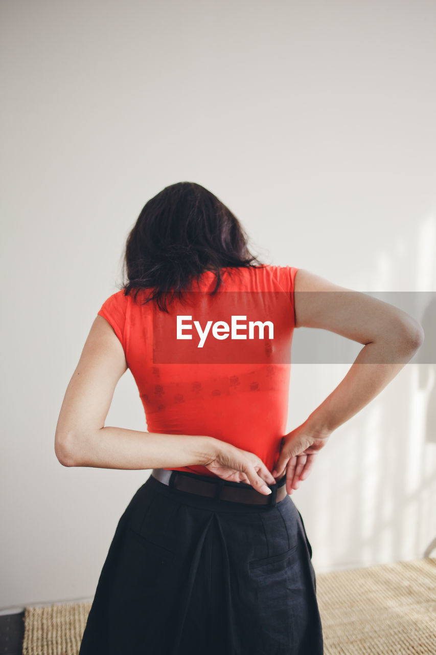 Rear view of woman standing against wall at home