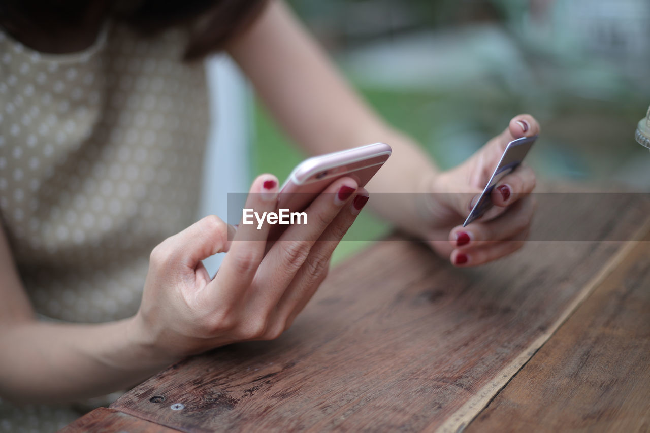 Midsection of woman using phone and credit card on table