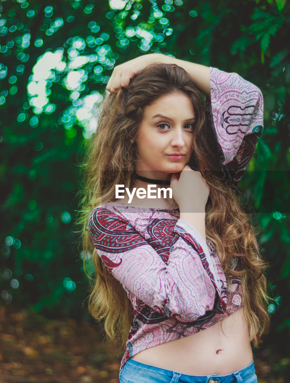 Portrait of beautiful young woman standing against trees