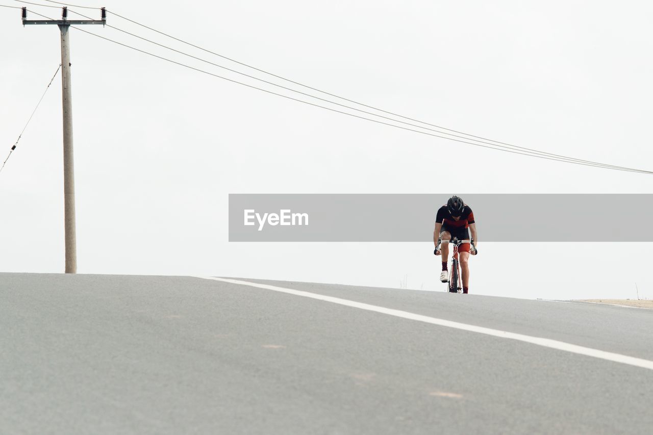 Man riding bicycle on road against clear sky