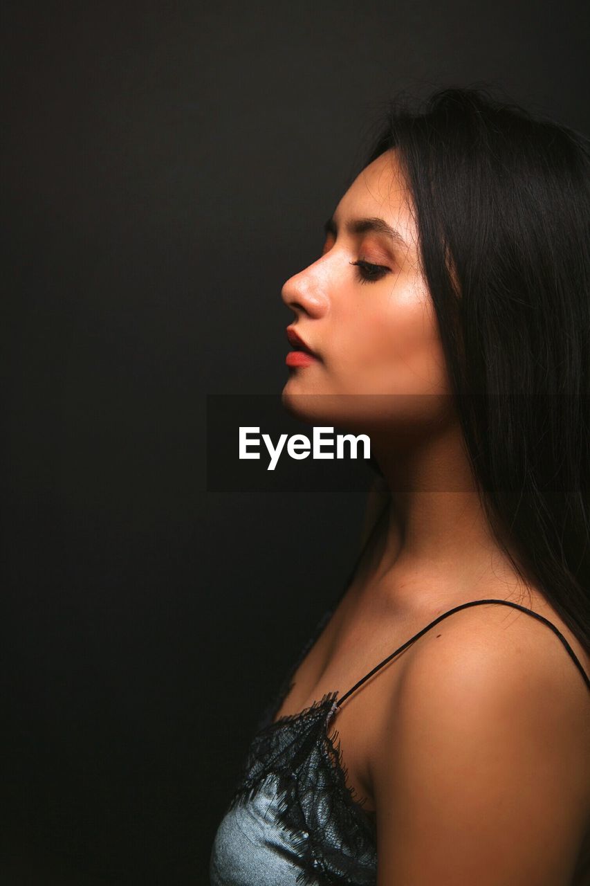 Profile view of beautiful woman standing against black background