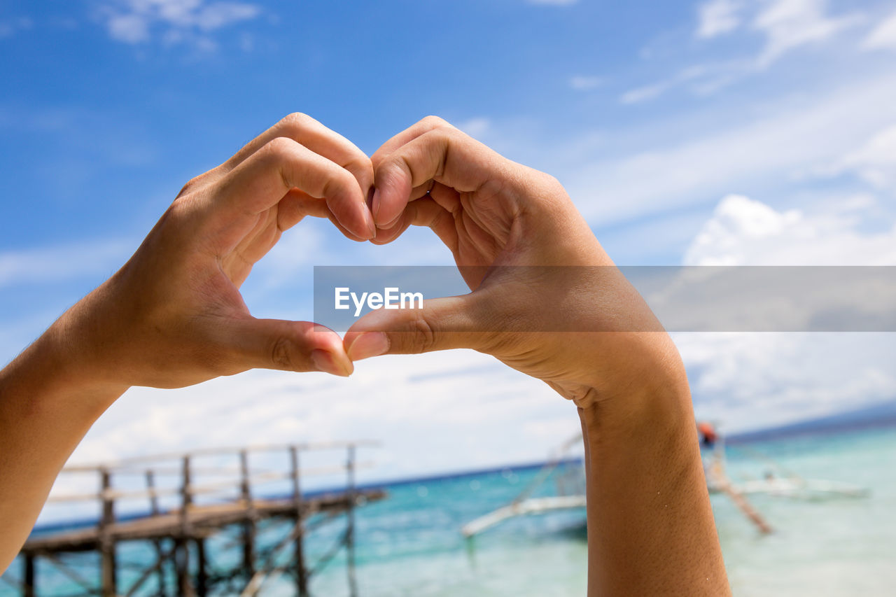 Close-up of hands making heart shape against sea