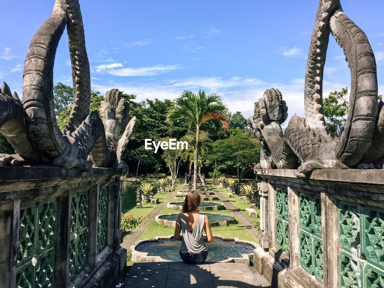 Rear view of woman sitting on steps amidst statues in park