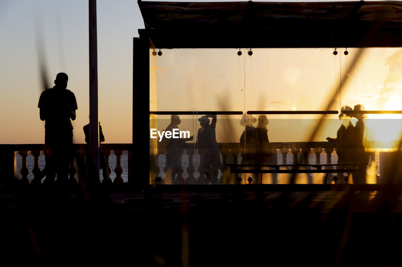 Silhouette at sunset of tree, bus stop and people walking on the edge of porto da barra.