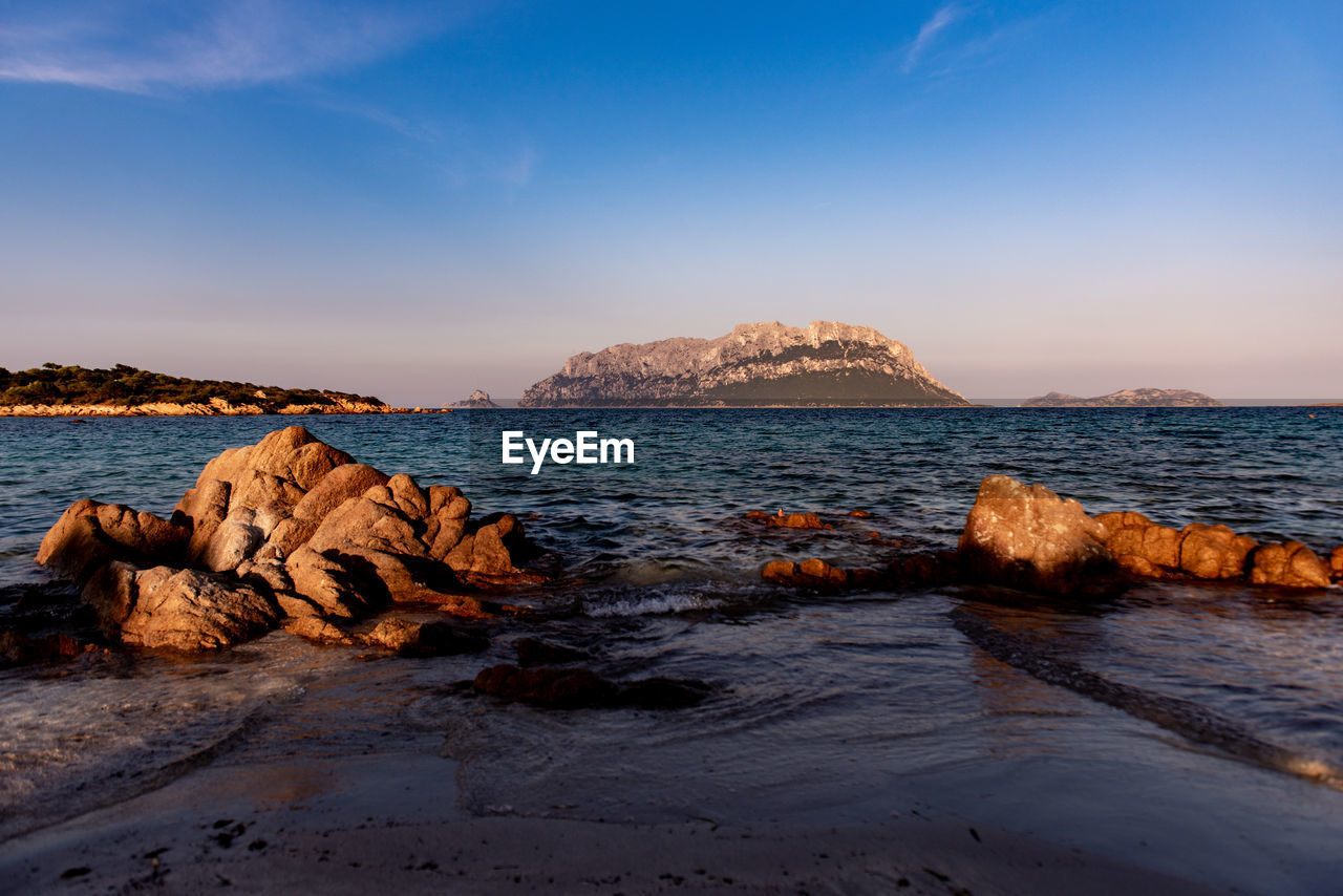 Rock formations on shore against blue sky