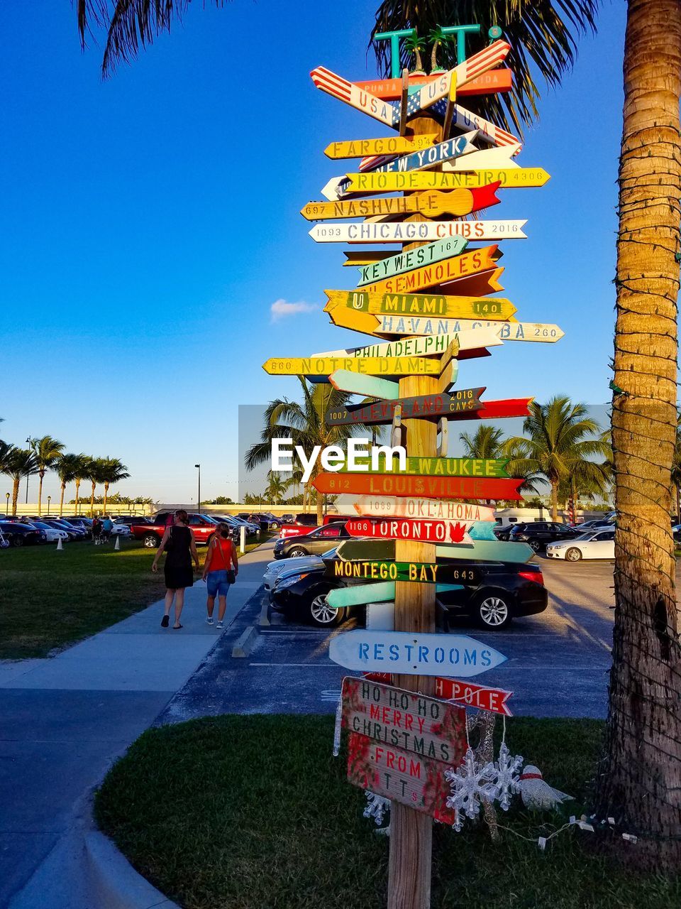 Marina sign with arrows pointing to different cities against palm trees and a clear sky