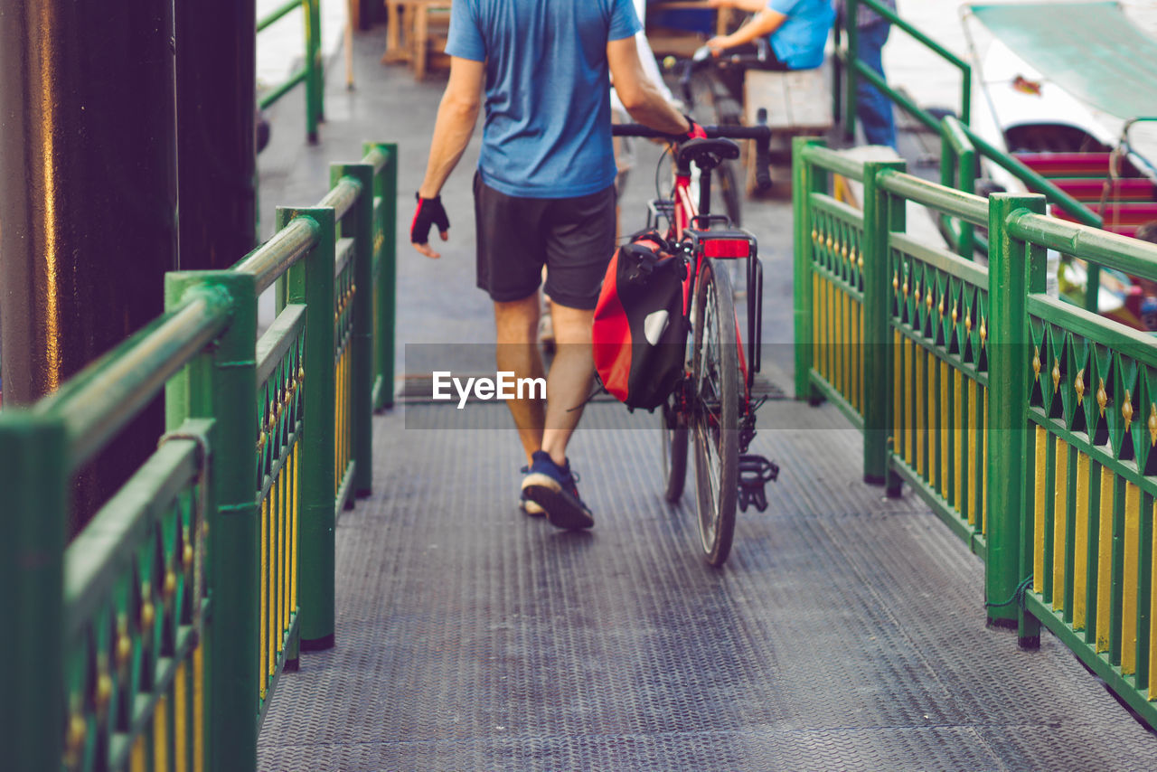 Low section of man with bicycle walking on footbridge