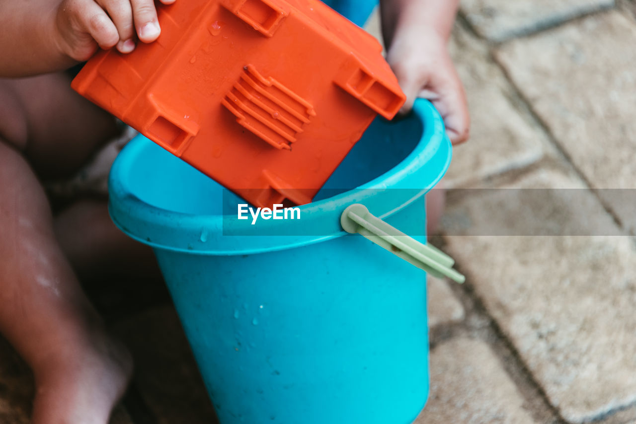 Low section of boy playing with bucket while sitting outdoors