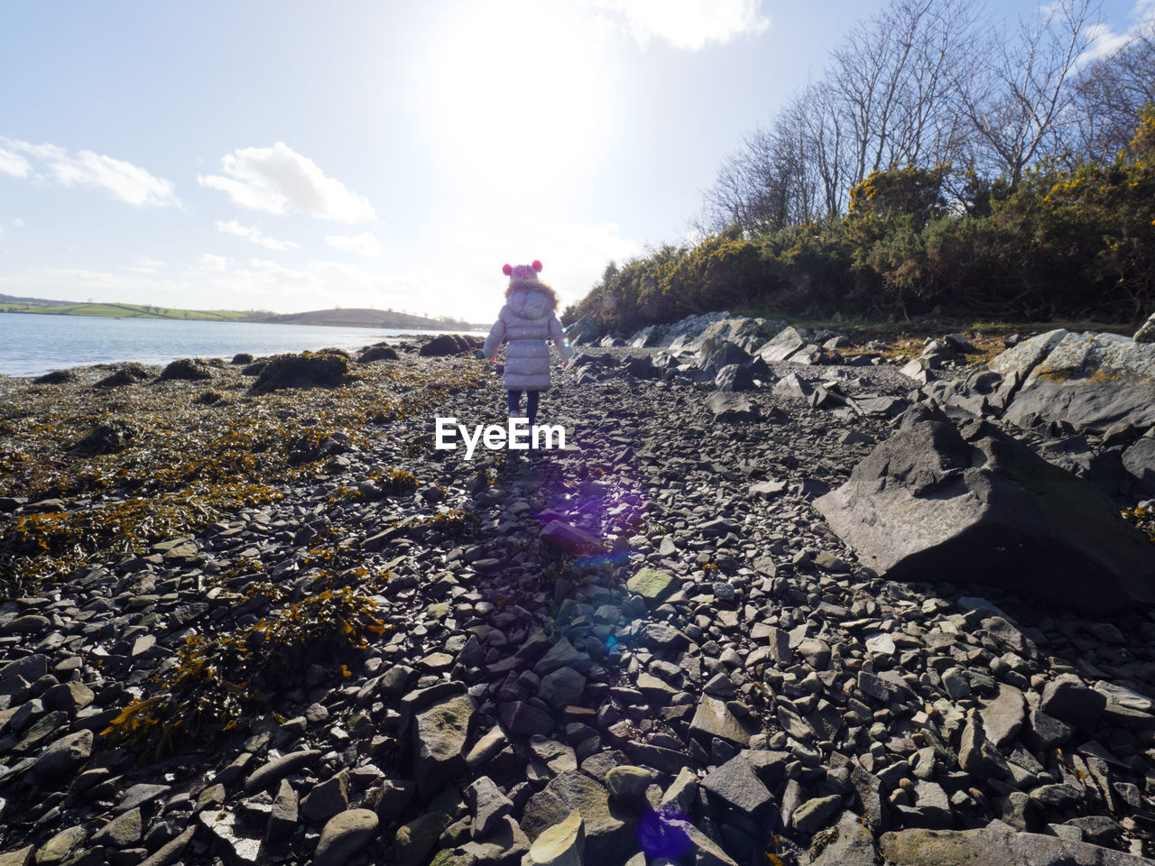 Young girl walking on rocks by sea against sky