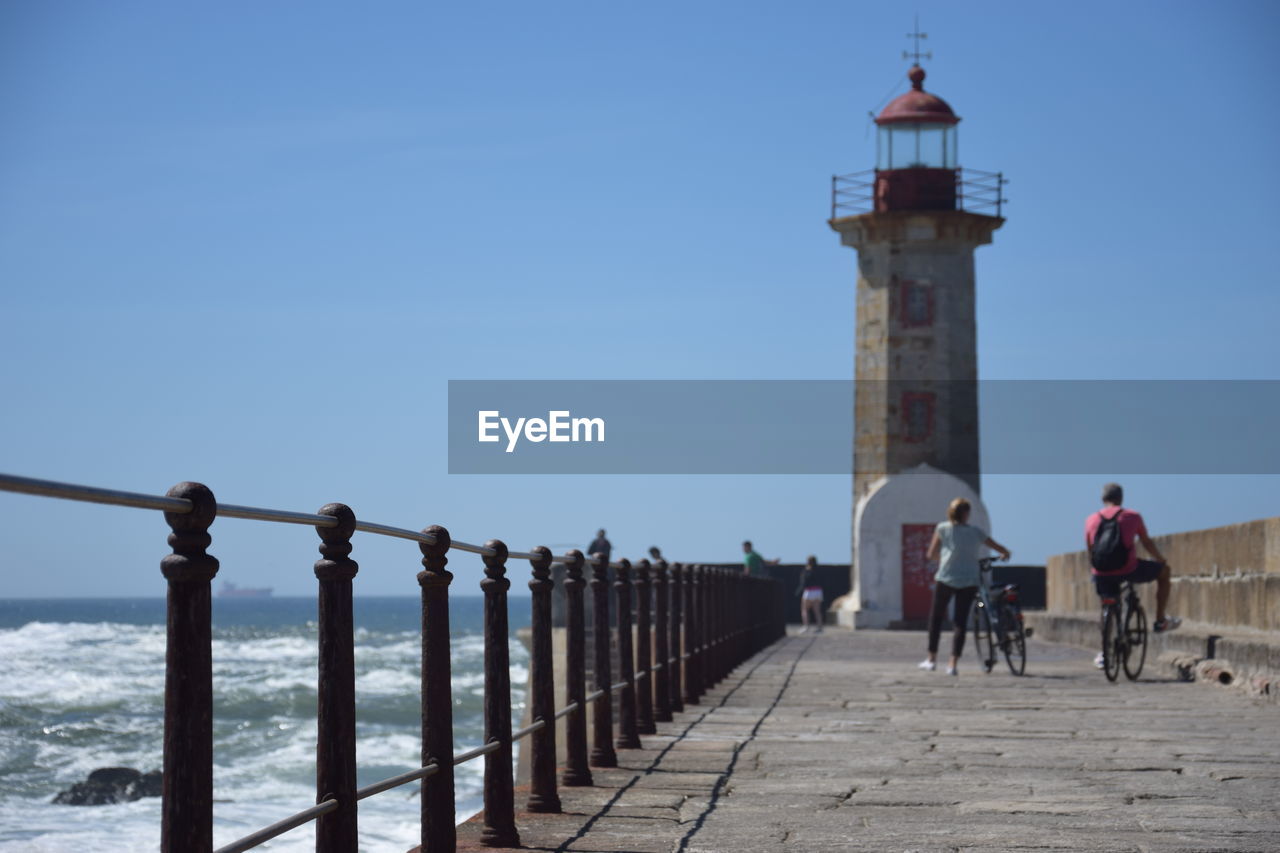 PEOPLE BY LIGHTHOUSE AGAINST SKY AND BUILDING