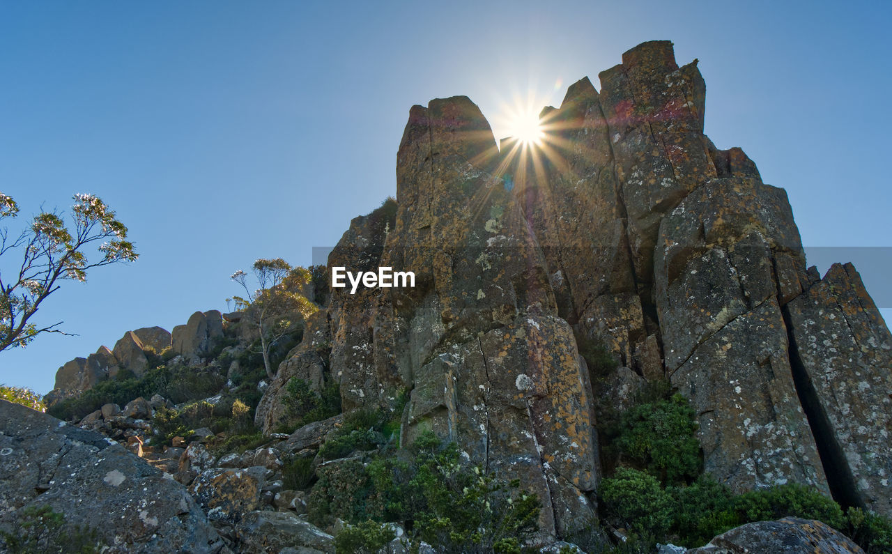 LOW ANGLE VIEW OF SUN SHINING ON ROCK AGAINST SKY