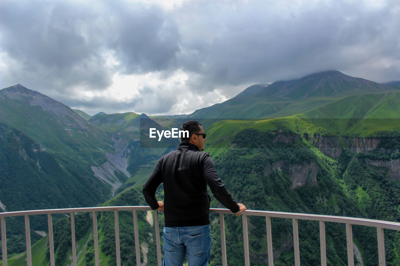 Rear view of man standing by railing against mountains