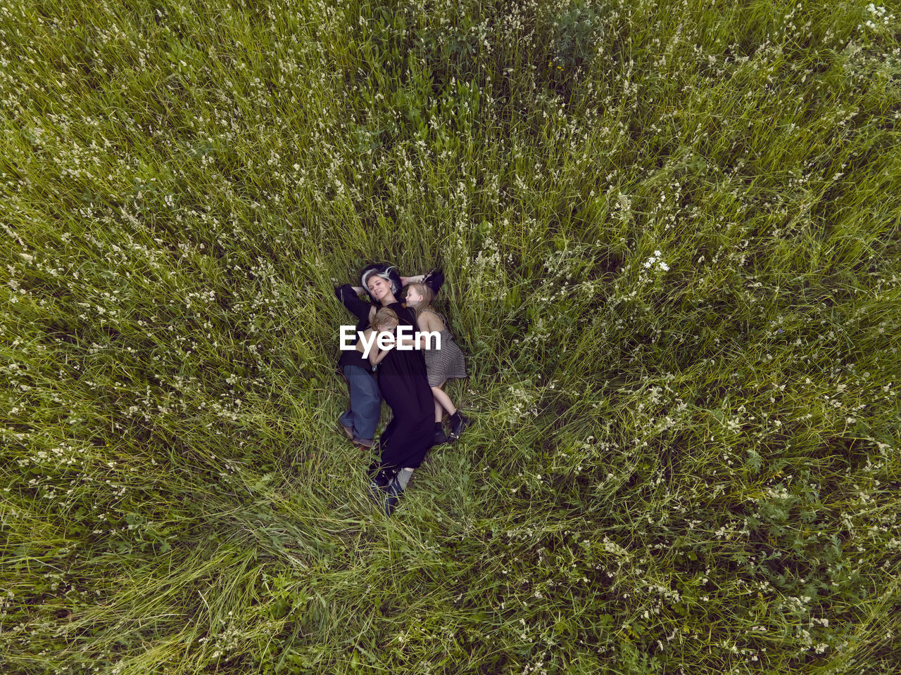 Mother in an evening dress with two daughters is lying on a green field with grass in the summer