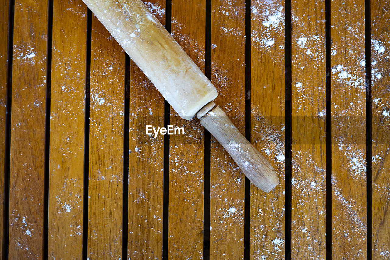 Wooden rolling pin with flour on a wooden background.
