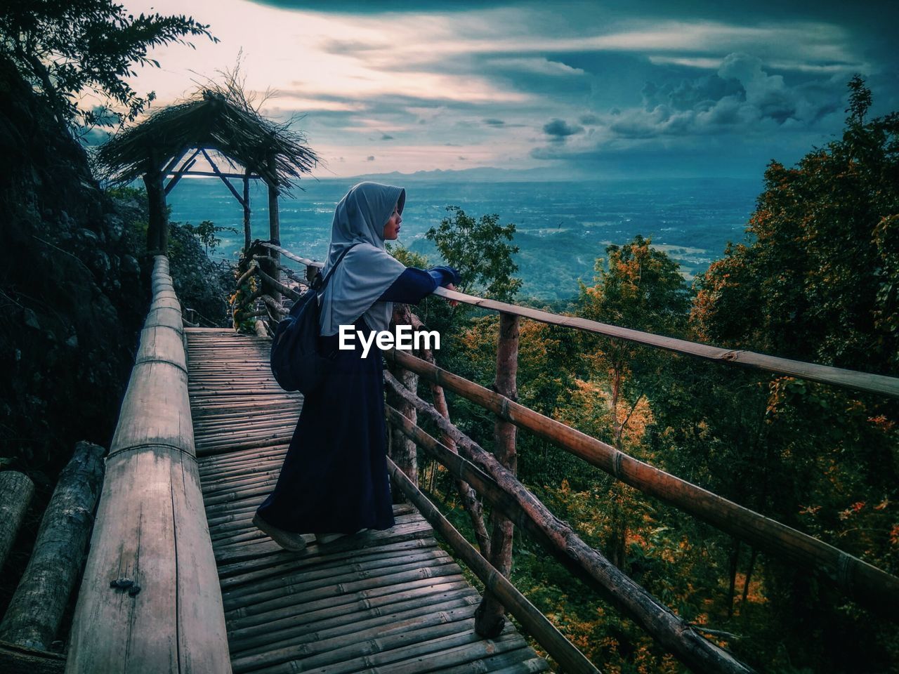 REAR VIEW OF WOMAN STANDING ON RAILING AGAINST TREES