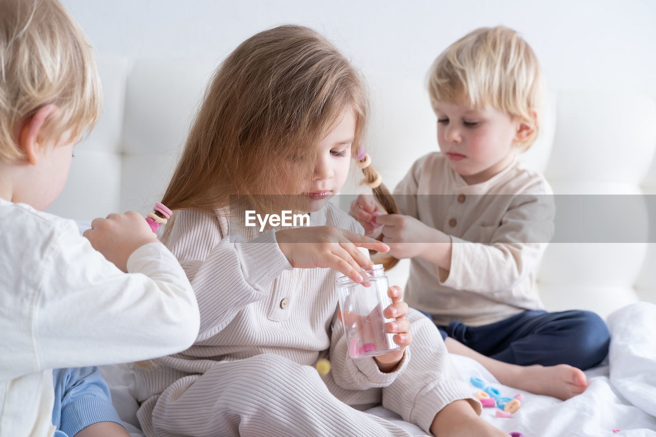 Cute boy tying sisters hair on bed at home