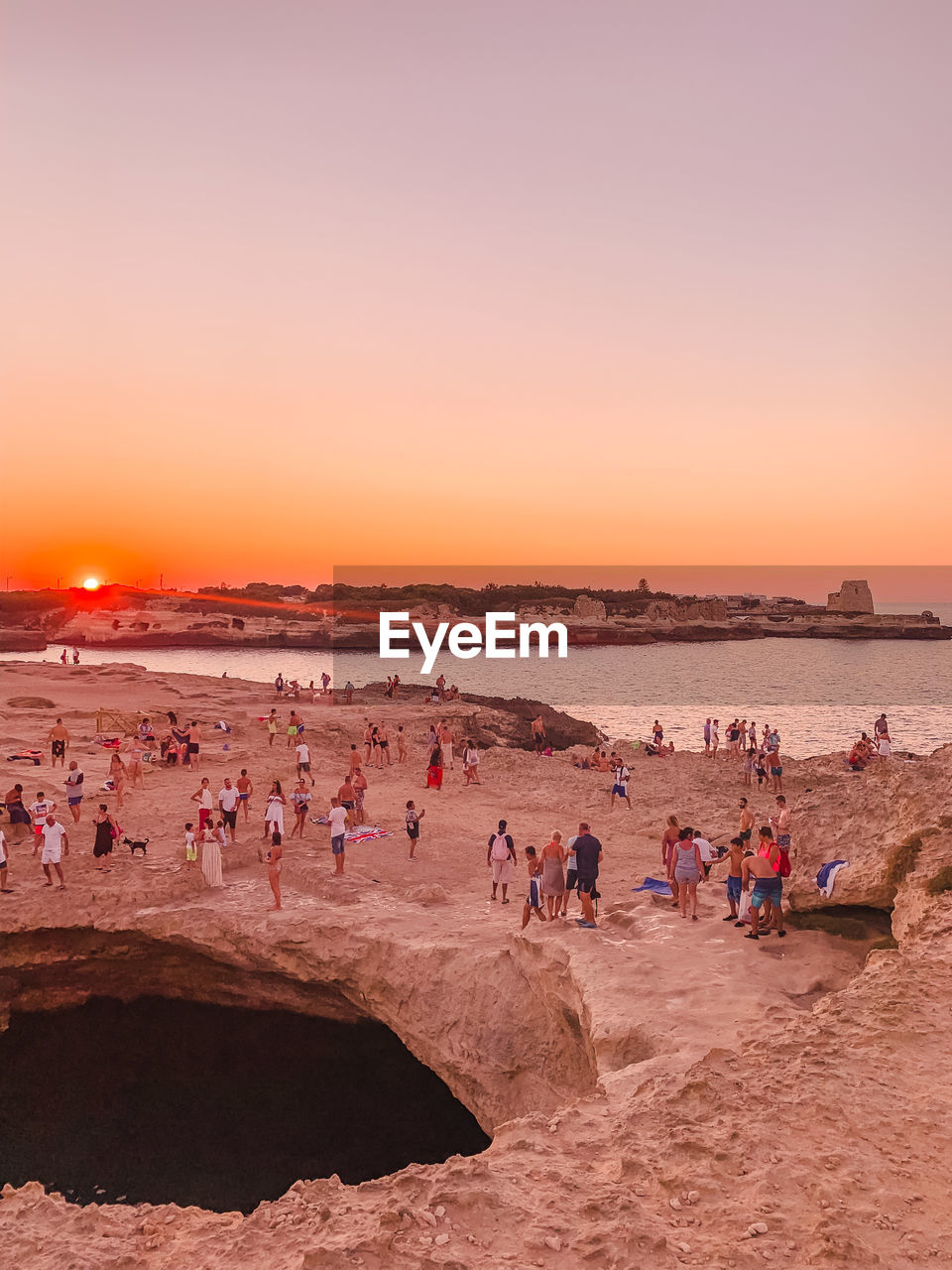 People at beach against clear sky during sunset