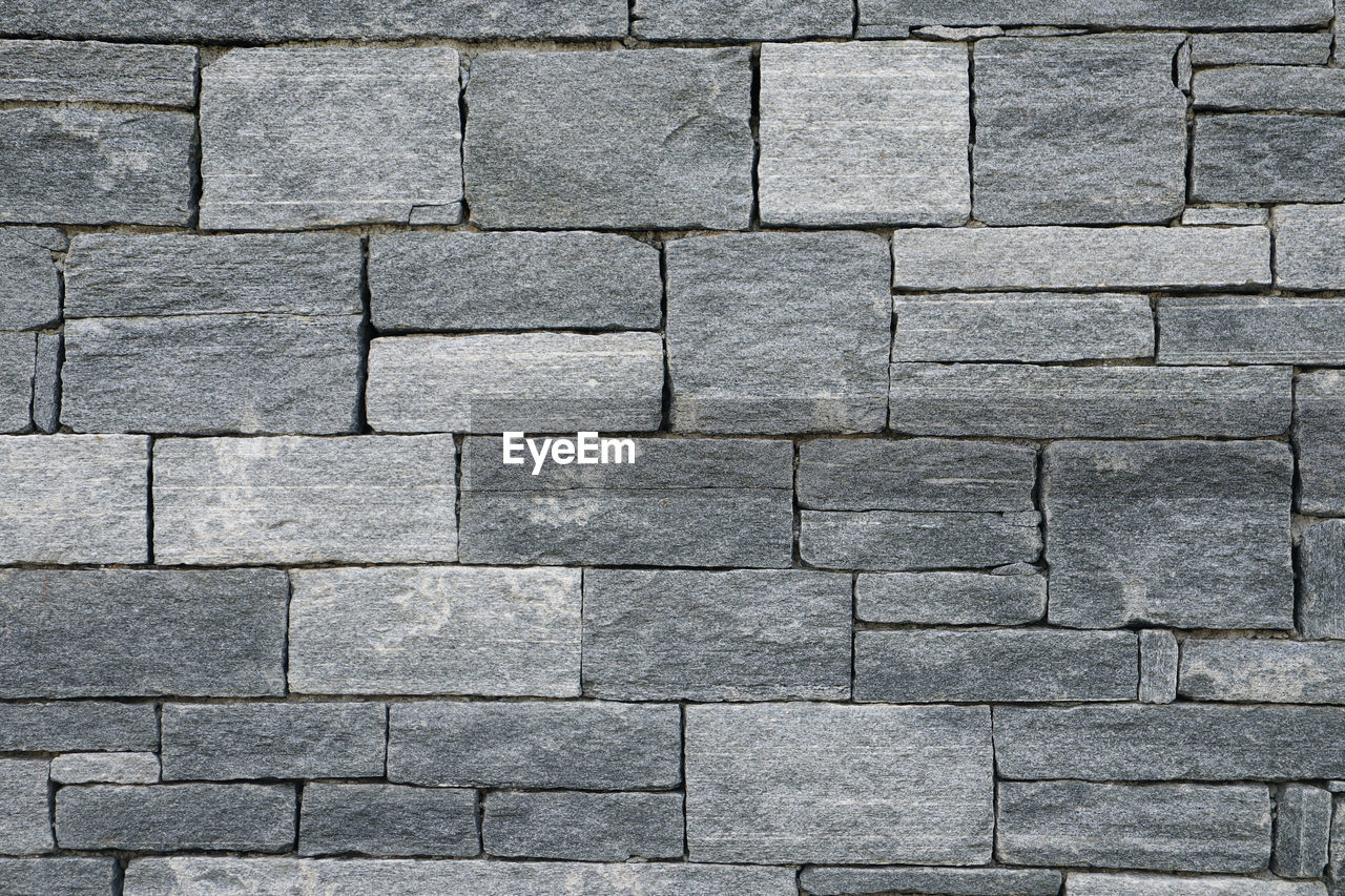 Big and small bricks in a grey stone wall