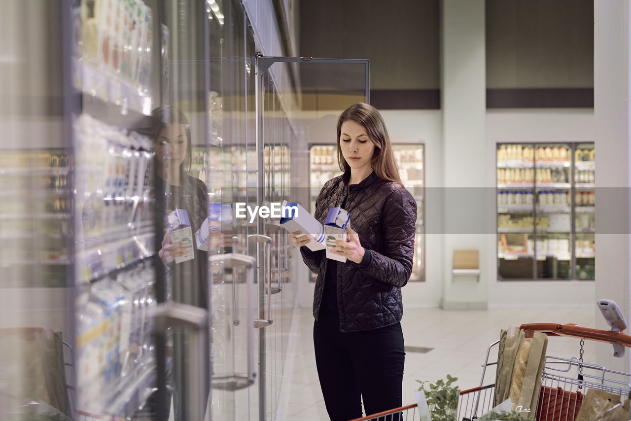 Woman holding juice boxes at refrigerated section in supermarket