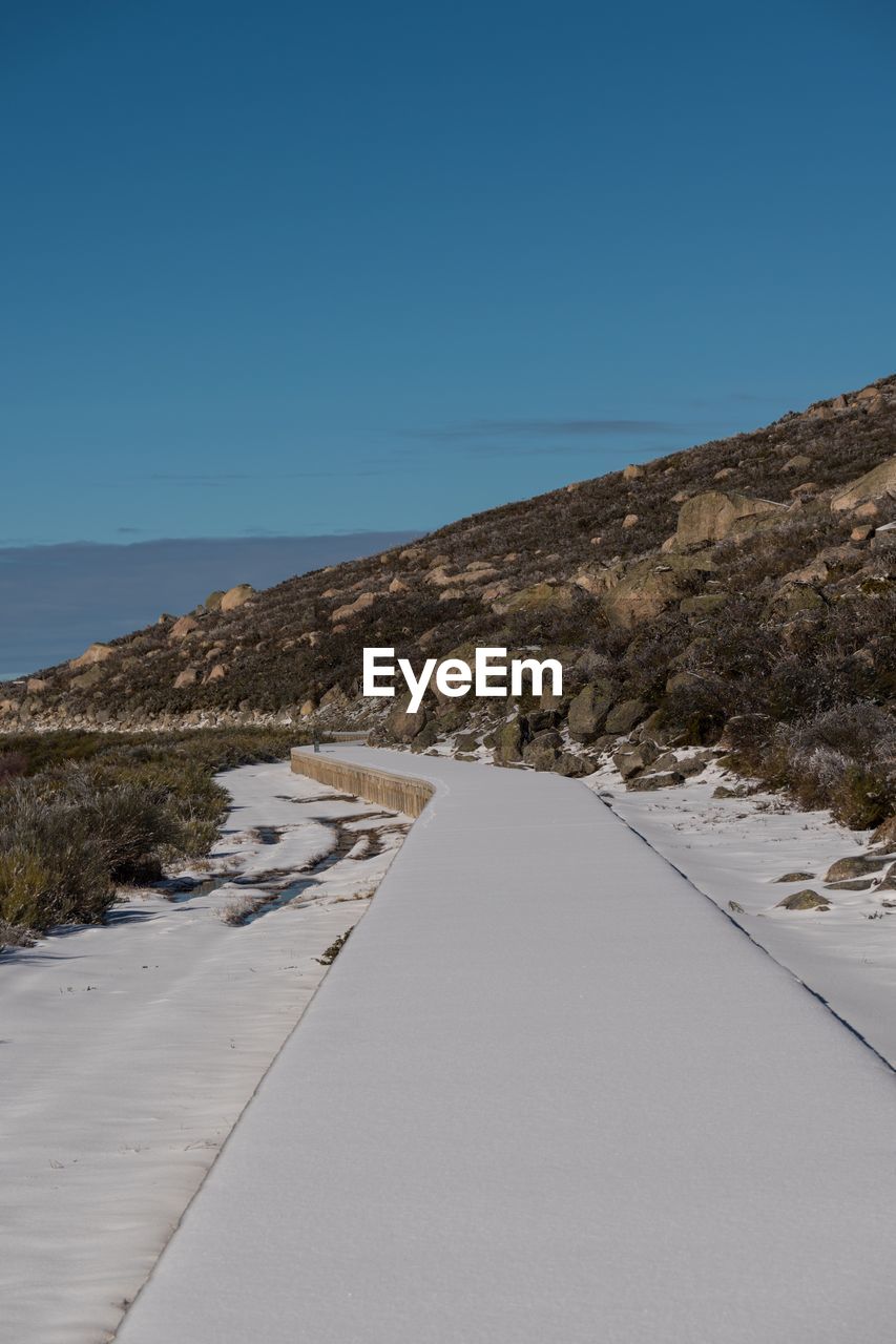 ROAD BY MOUNTAINS AGAINST CLEAR BLUE SKY