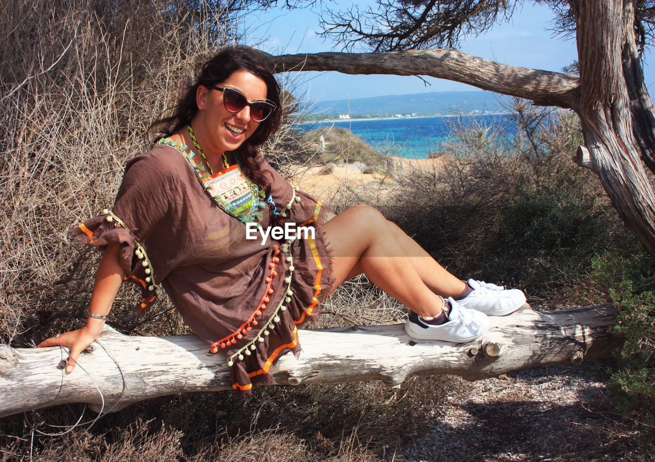 Young caucasian brunette woman on vacation with traditional dress sitting on a tree trunk in ibiza