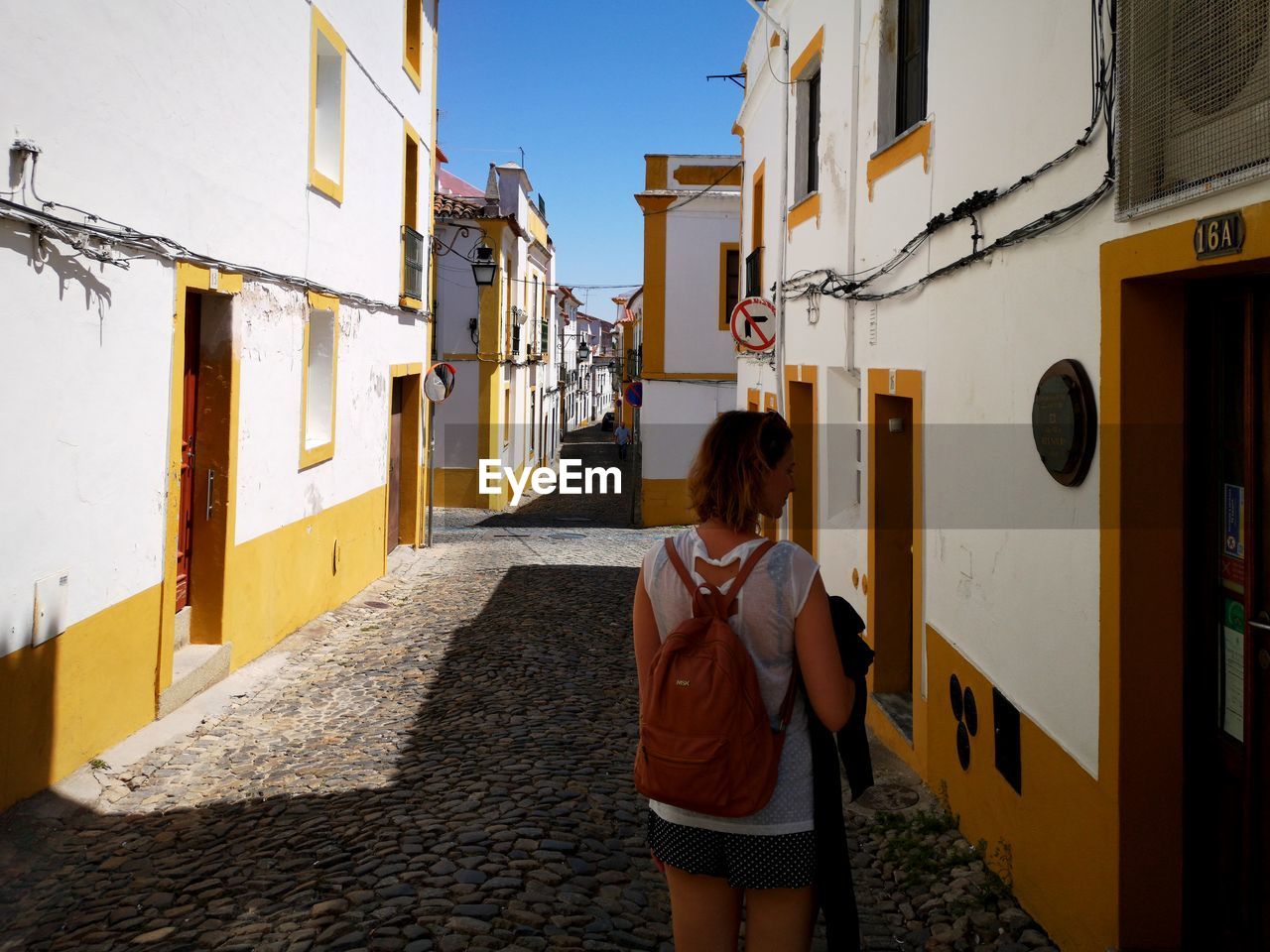 REAR VIEW OF WOMAN STANDING ON STREET AGAINST BUILDINGS