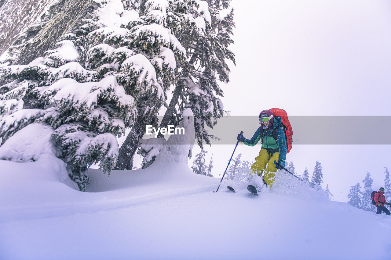 Woman jumping from top of snowy hill while backcountry skiing in bc
