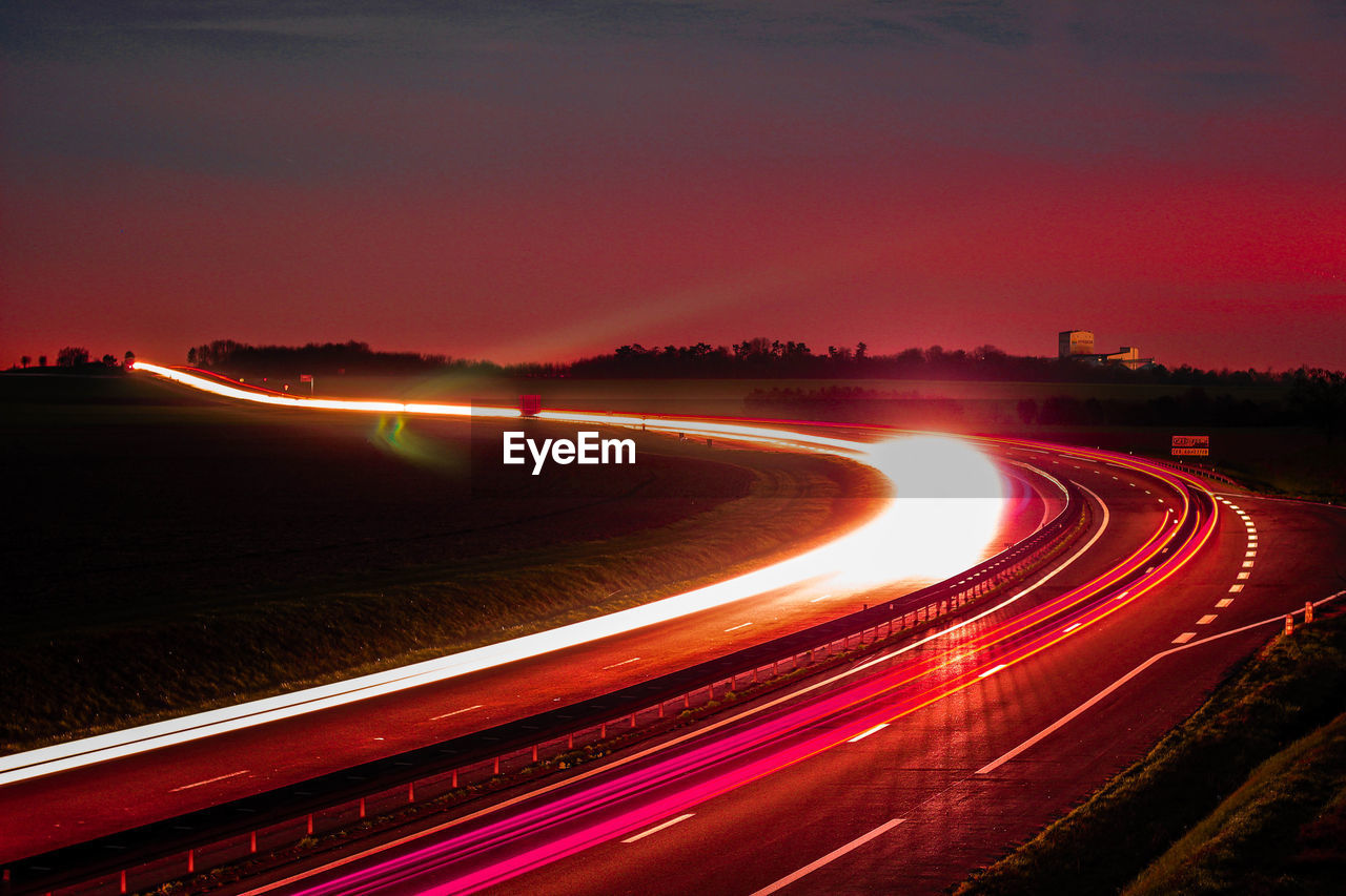 LIGHT TRAILS ON ROAD IN CITY AGAINST SKY AT NIGHT