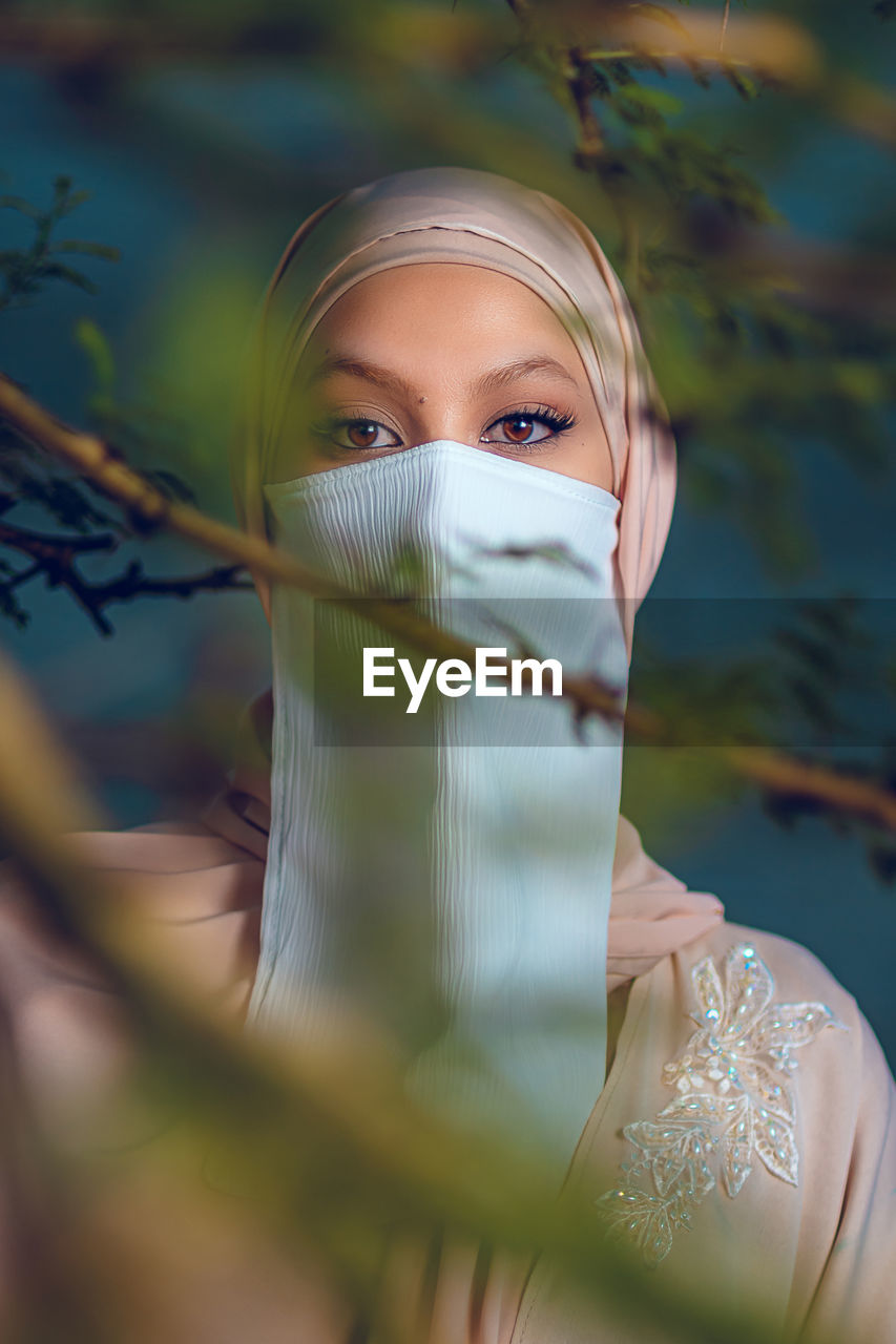 Portrait of veiled woman with white niqab and hijab standing behind the tree