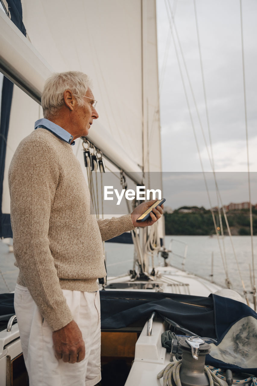 Senior man navigating direction through smart phone while standing on boat during sunset