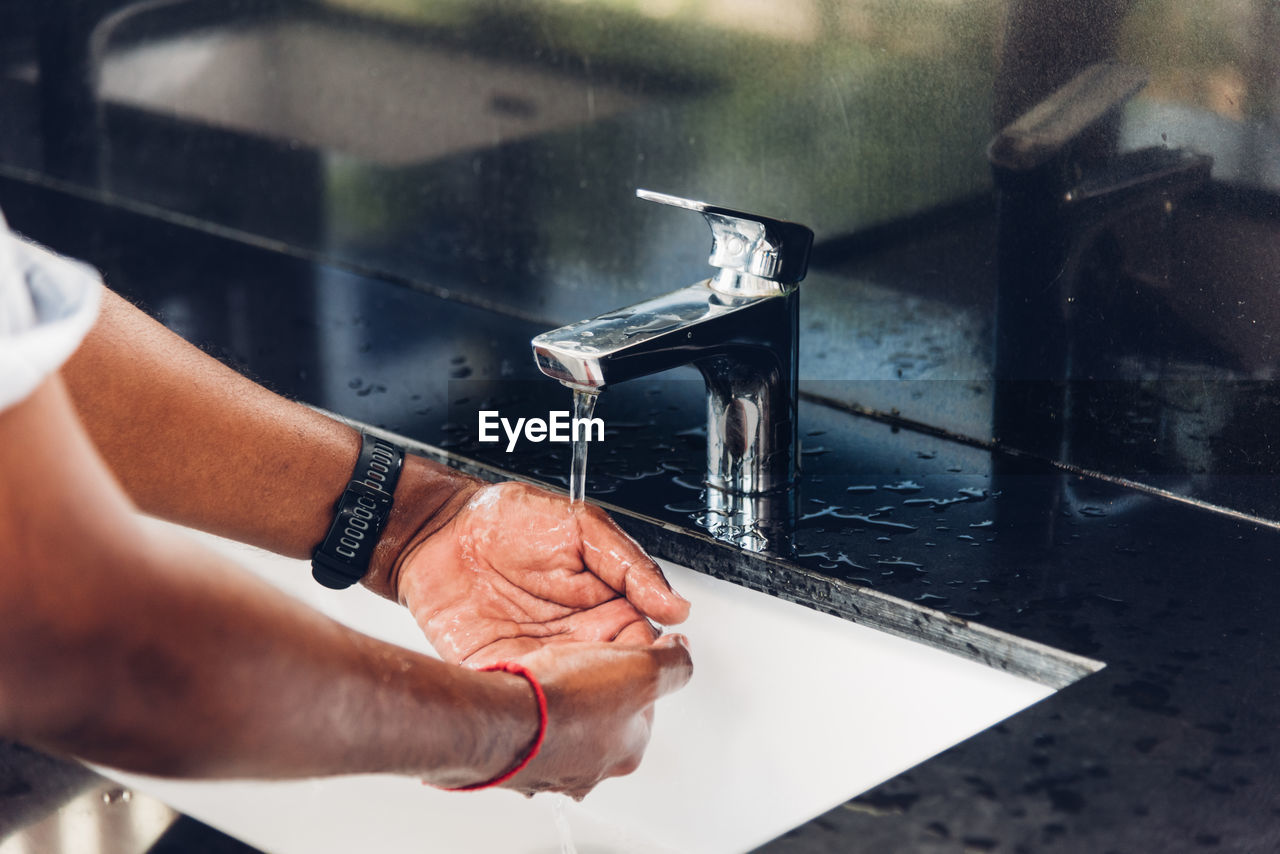 cropped hand of person washing hands in sink