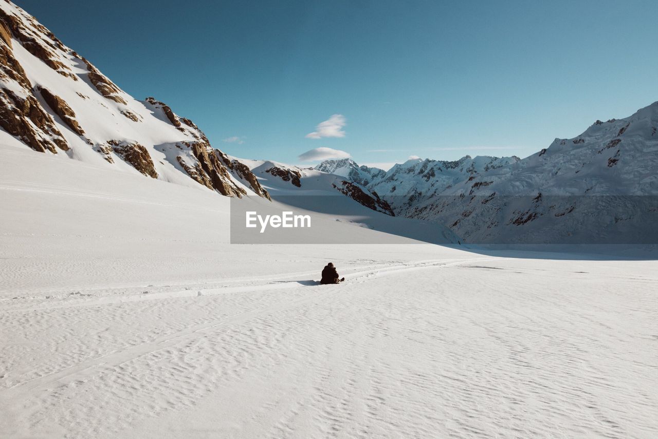 Rear view of person sitting on snowcapped mountain against sky