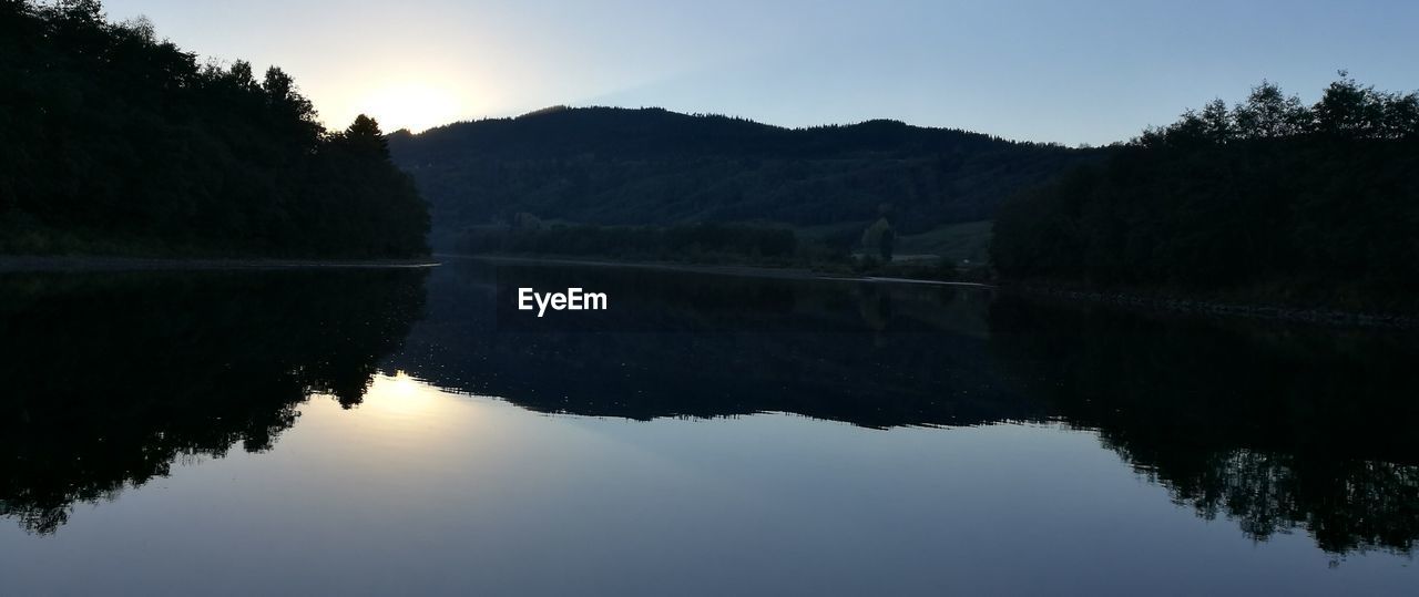 CALM LAKE WITH SILHOUETTE MOUNTAIN RANGE IN BACKGROUND