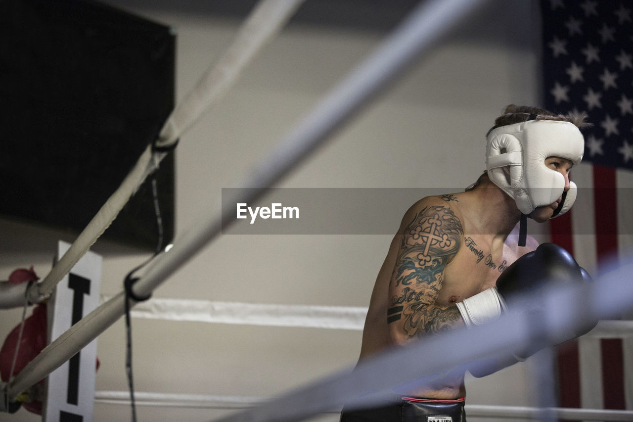 Shirtless boxer practicing in boxing ring at gym