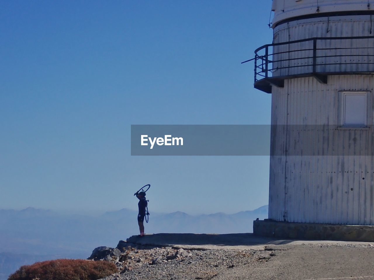 tower, lighthouse, sky, architecture, blue, built structure, one person, nature, sea, building exterior, standing, day, men, clear sky, land, full length, coast, water, adult, beach, outdoors, mountain, protection, security, scenics - nature, copy space, building, industry, guidance