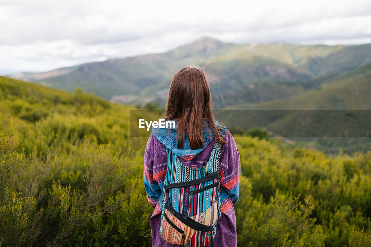 Young woman with alternative clothes looking at a big green mountain