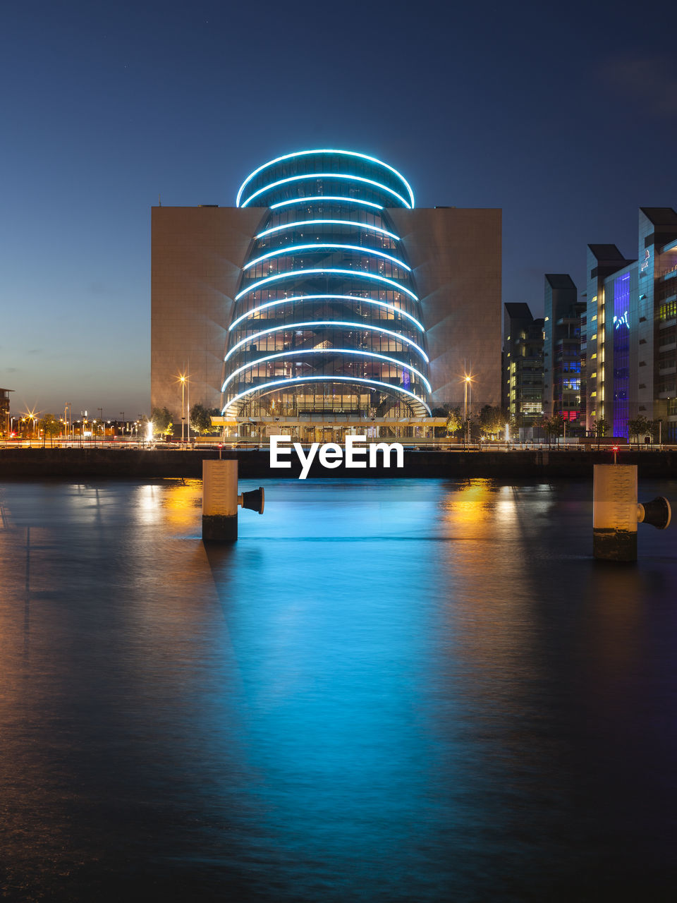 Illuminated buildings by river against sky at night