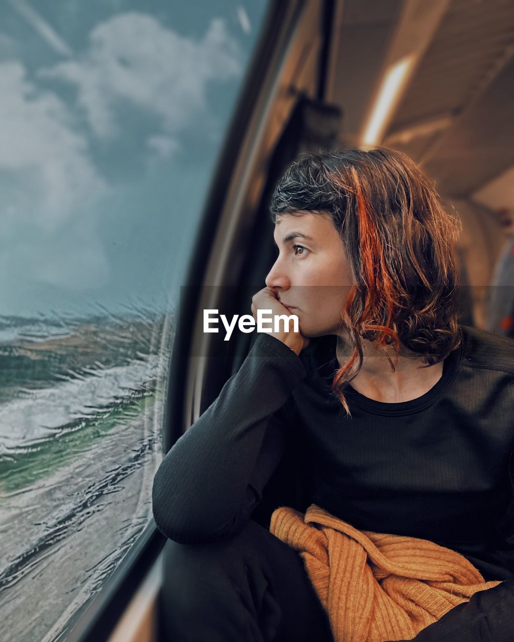 YOUNG WOMAN LOOKING AWAY WHILE SITTING IN CAR WINDOW