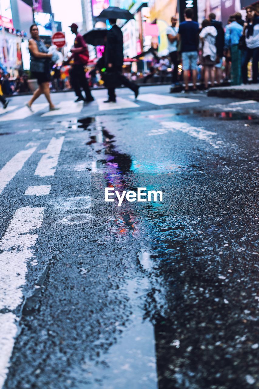 Reflection of people walking on illuminated street in puddle at night