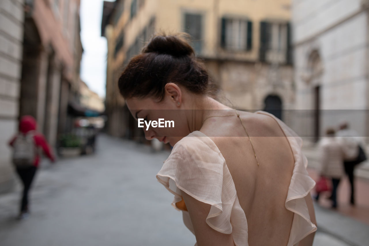 Rear view of woman looking down while walking on street in city